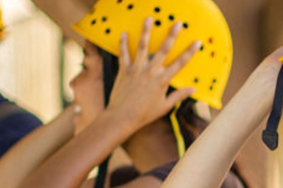 People wearing yellow safety helmets and harnesses, preparing for an outdoor activity in a wooden structure.