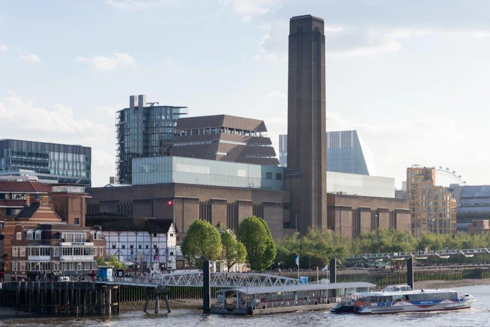 A riverside view of the Tate Modern art gallery in London, with the Globe Theatre and boats on the Thames in the foreground.