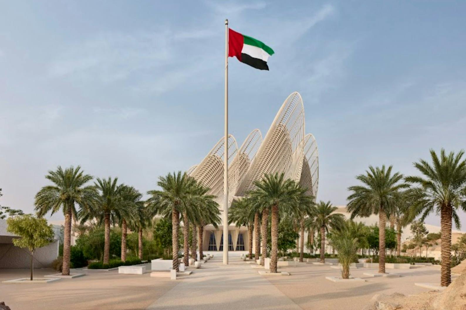 야자수로 둘러싸인 현대적인 건축 양식의 건물로, 아랍에미리트 국기가 전면에 배치되어 있습니다.