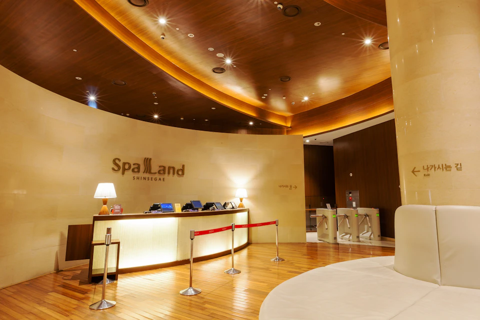Reception area of Spa Land Shinsegae with a curved wooden ceiling, front desk, and turnstiles in a modern setting.