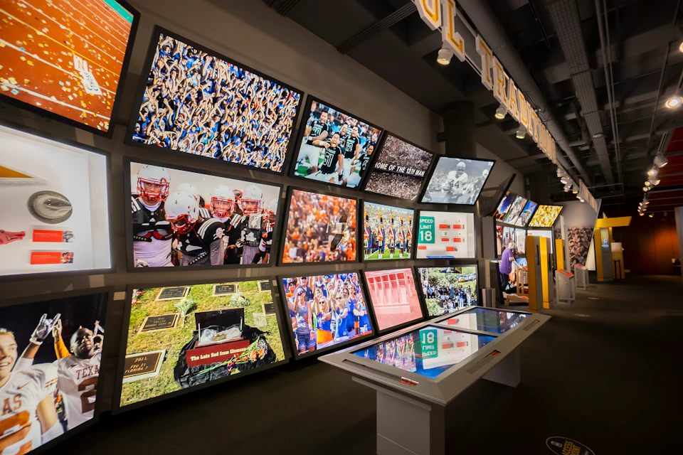 A wall of various sports images and videos displayed on large screens, with a touchscreen table in the foreground.