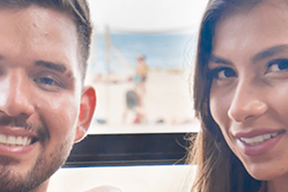 A man and woman smiling at a table with a champagne bottle in an ice bucket, set against a beachside background.