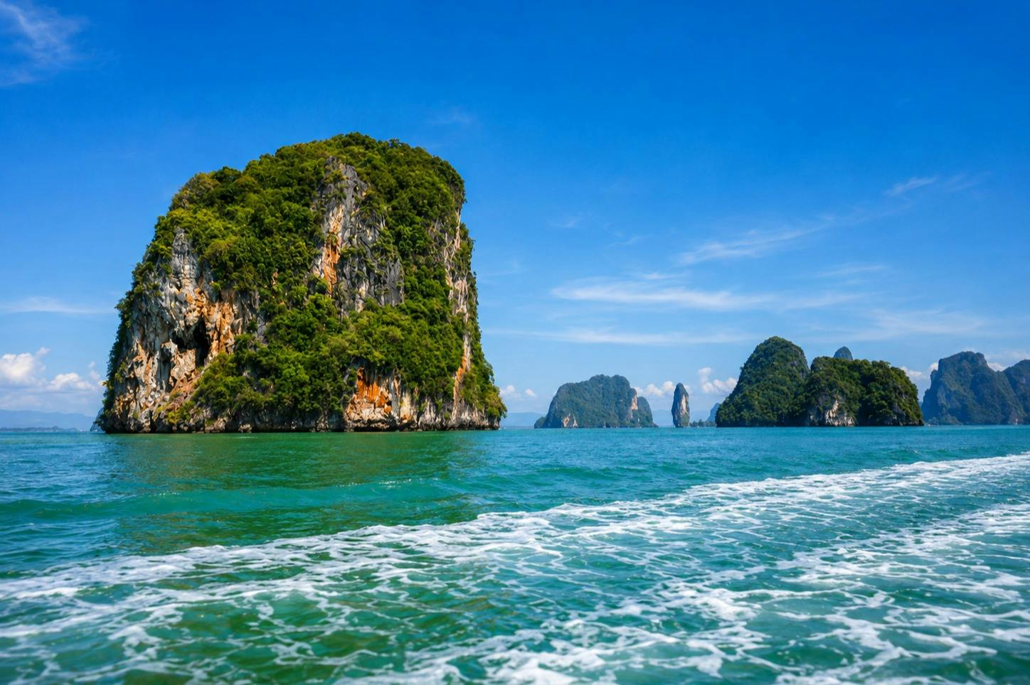 A scenic view of limestone islands covered in greenery rising from turquoise waters under a clear blue sky.