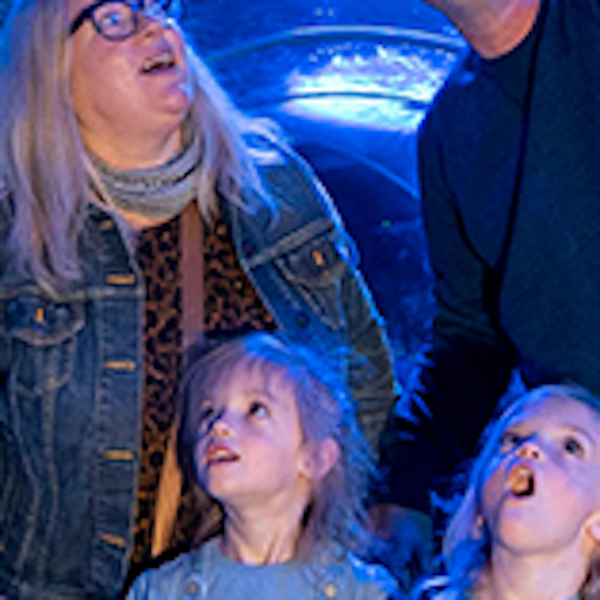 A family with three children looks up at a shark swimming in an underwater tunnel at an aquarium.