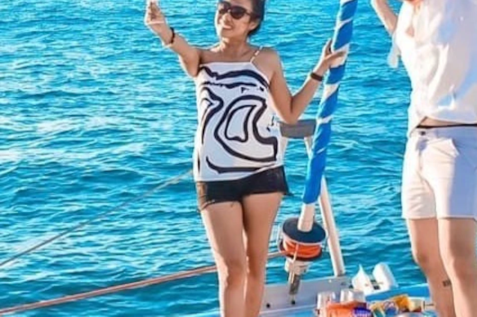 Four people on a boat in the ocean, smiling and holding drinks, with a clear blue sky and distant land in the background.