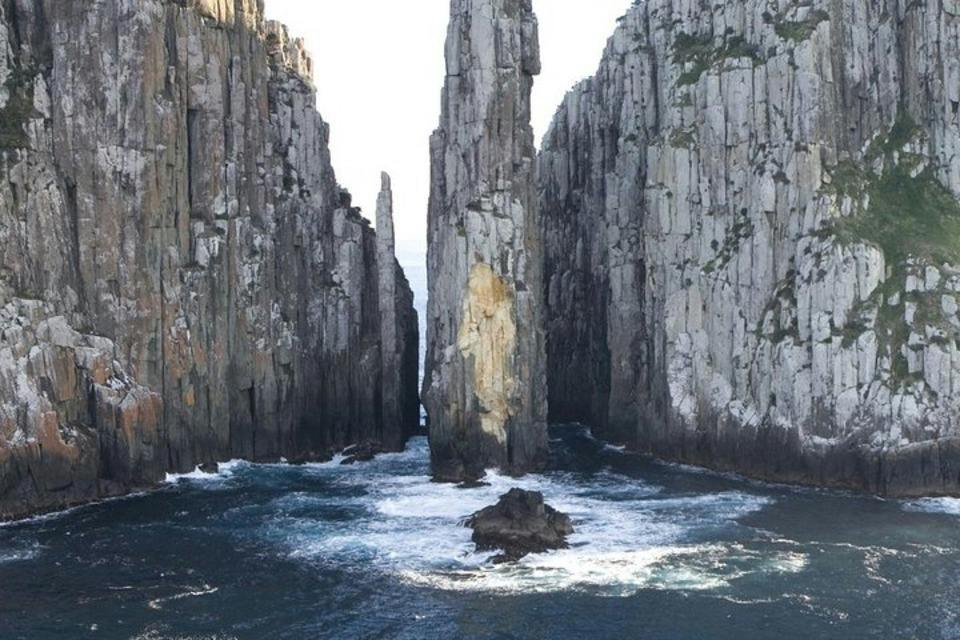 Tall rocky cliffs with sharp vertical formations rise from the ocean, with waves crashing against the rocks below.