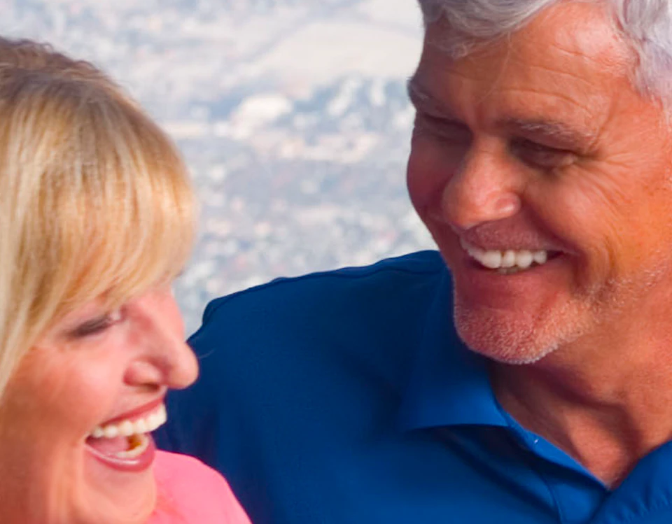 A couple enjoys a meal at an outdoor table with a scenic mountain and valley view in the background.