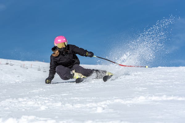 Person in black clothing and pink helmet skiing sharply on a snowy slope under a bright blue sky.