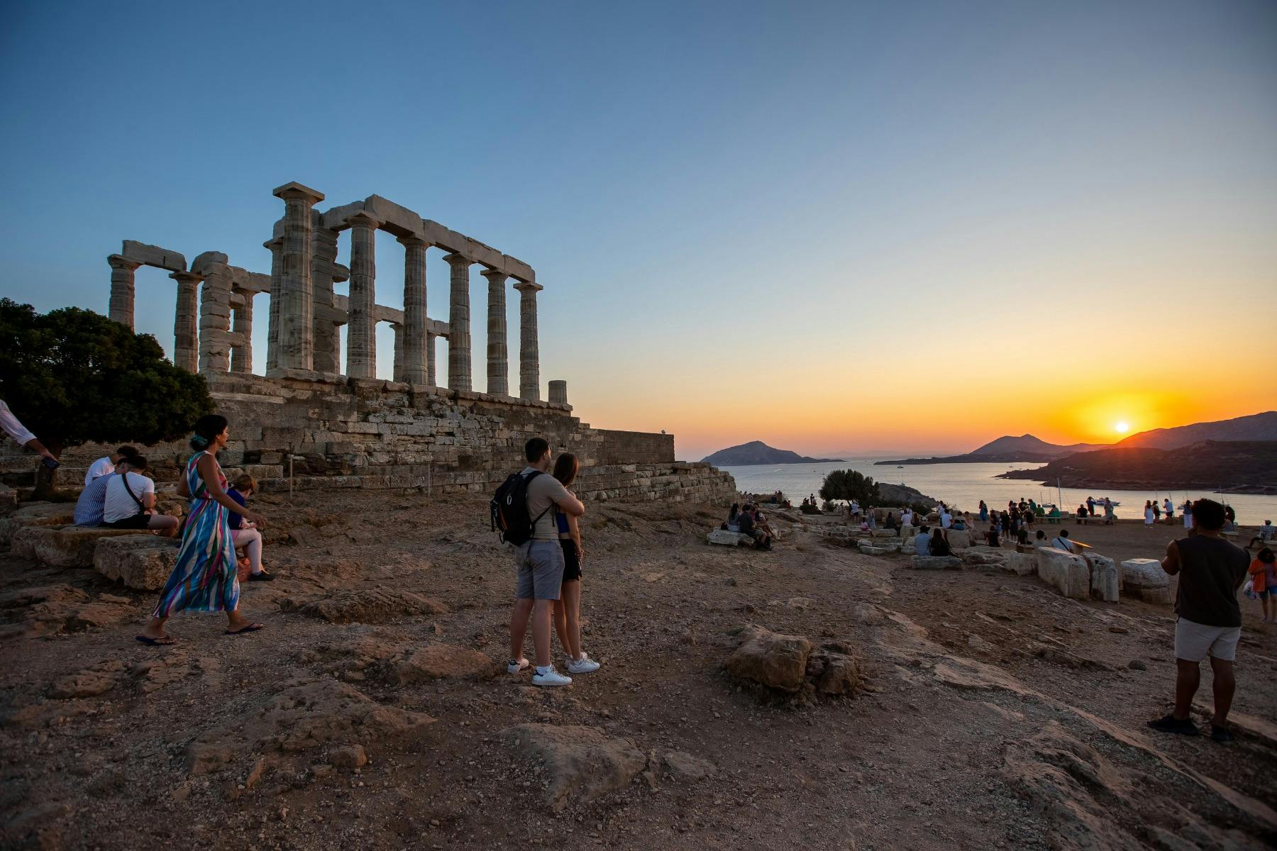 Couples and visitors enjoying the sunset next to the Temple of Poseidon at Cape Sounion.