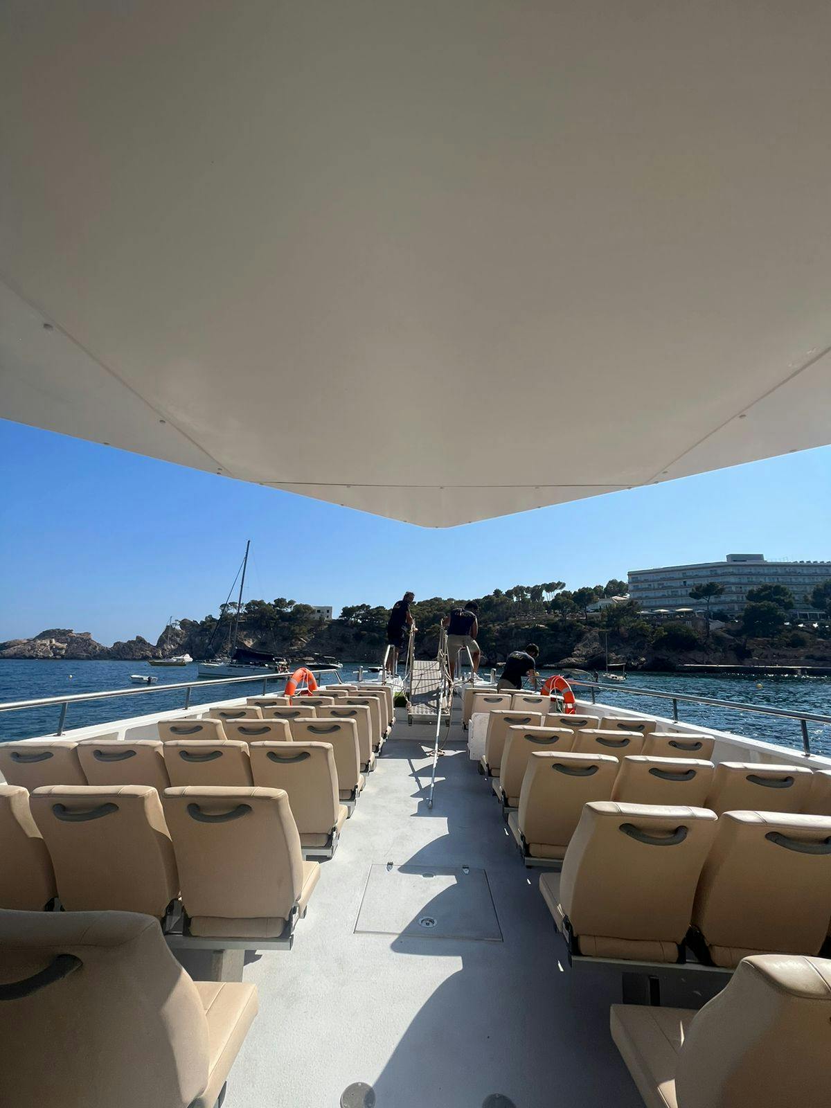 Άδεια καθίσματα σε μια βάρκα με κάλυμμα οροφής, με θέα μια ήρεμη θάλασσα, μια μακρινή ακτογραμμή με δέντρα και έναν καταγάλανο ουρανό.