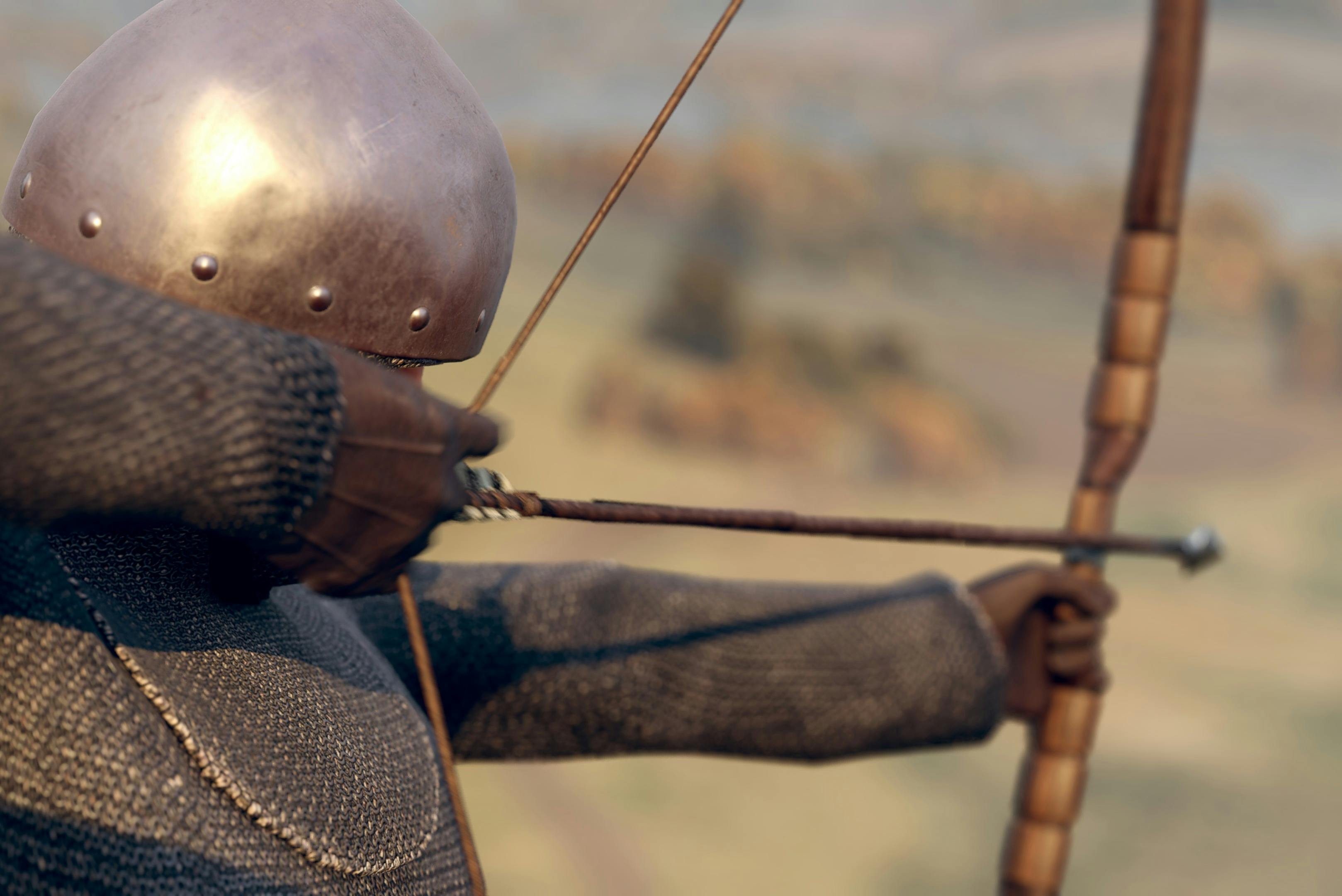 Średniowieczny łucznik w kolczugach i hełmie wyciągający łuk, celujący w dal.