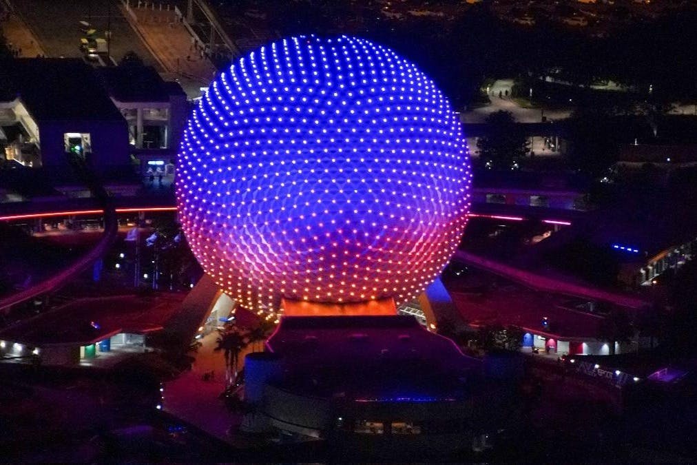 Large geodesic sphere illuminated with purple and red lights at night, with surrounding structures and pathways visible.
