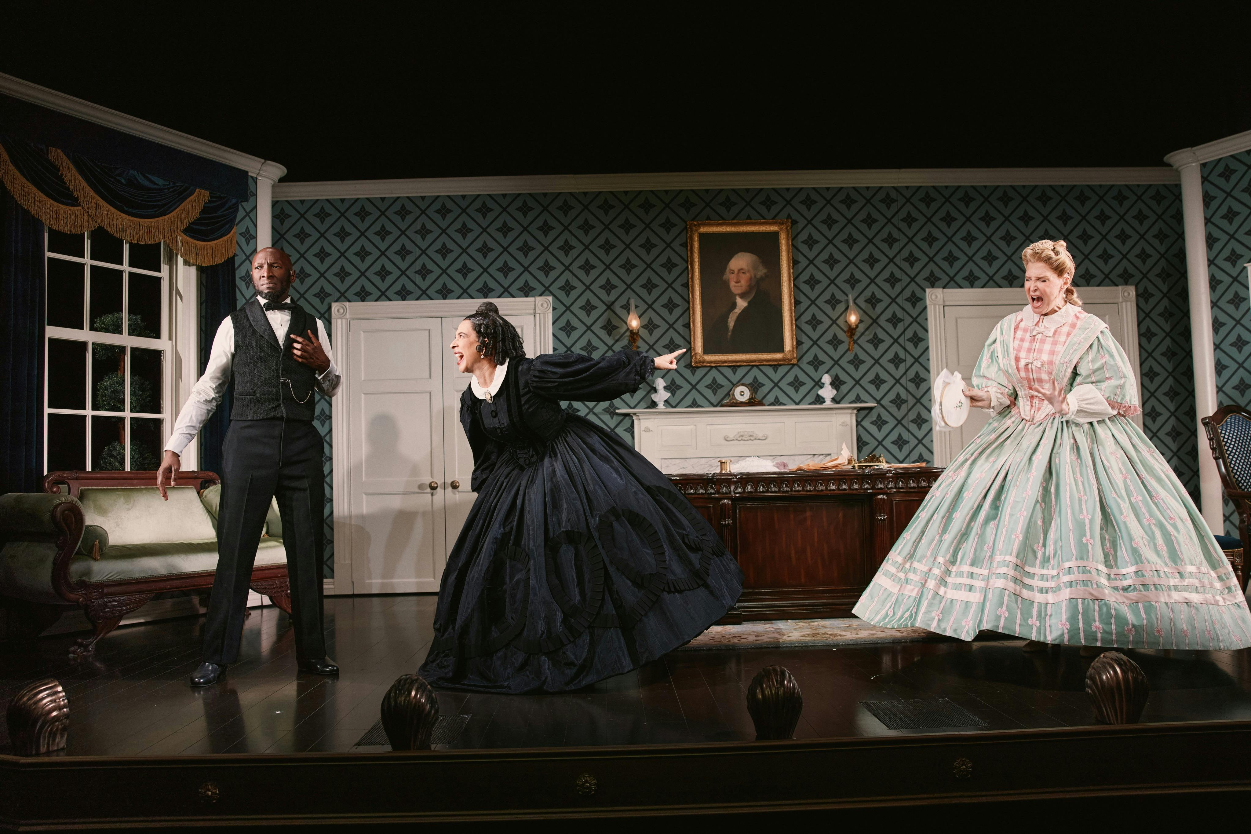 Two women in period costumes, one in black and the other in green, performing dramatically on a stage with a vintage decor.