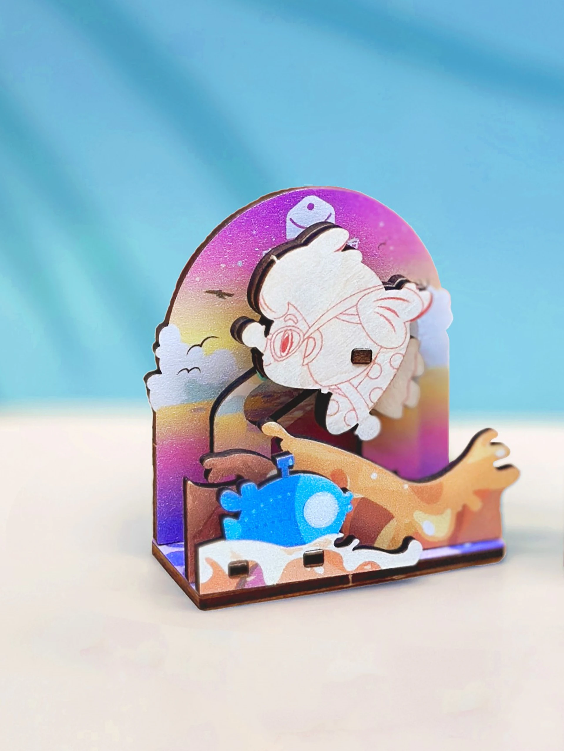 A colorful wooden figurine with a sky-themed background and whimsical shapes, including a character and abstract forms.
