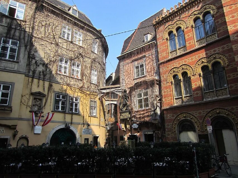Three historic buildings with intricate facades and numerous windows surround a small courtyard under a clear blue sky.