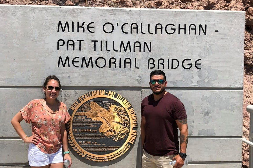 Two people stand in front of a wall with the &#34;Mike O&#39;Callaghan-Pat Tillman Memorial Bridge&#34; inscription and a commemorative plaque.