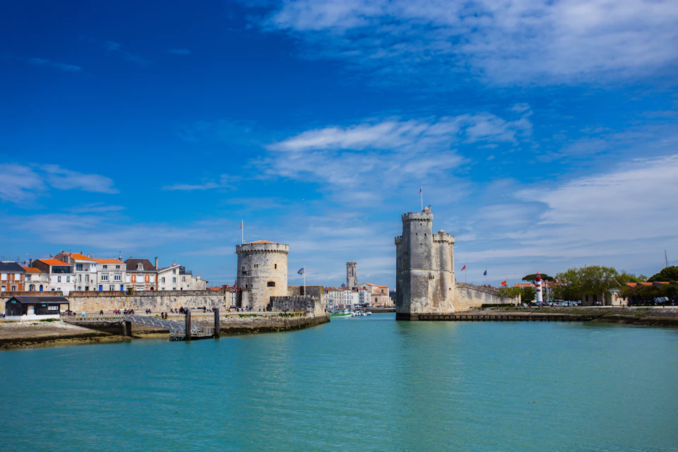 Historical towers and waterfront buildings under a bright blue sky by a calm, turquoise waterway.