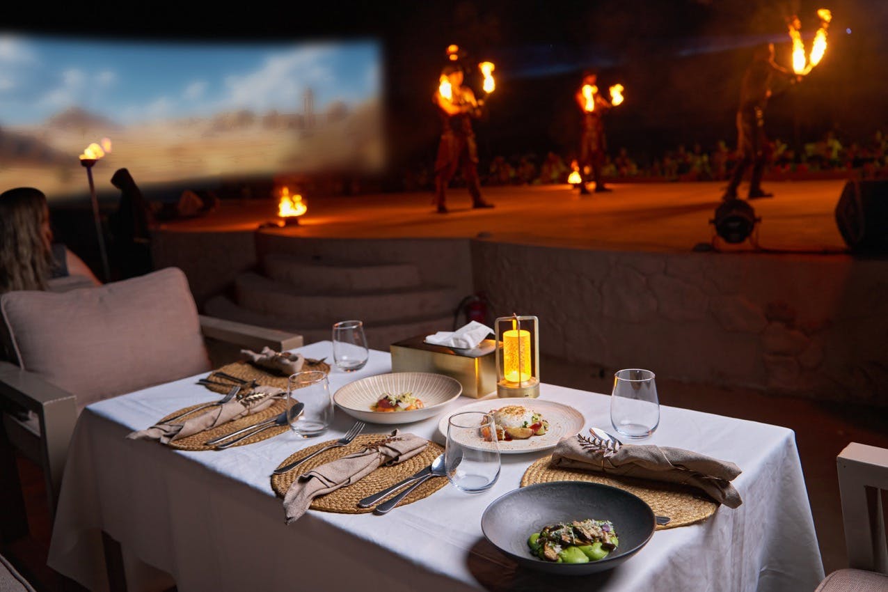 Een tafel met borden eten tegenover een podium waar artiesten vuur hanteren voor een publiek.