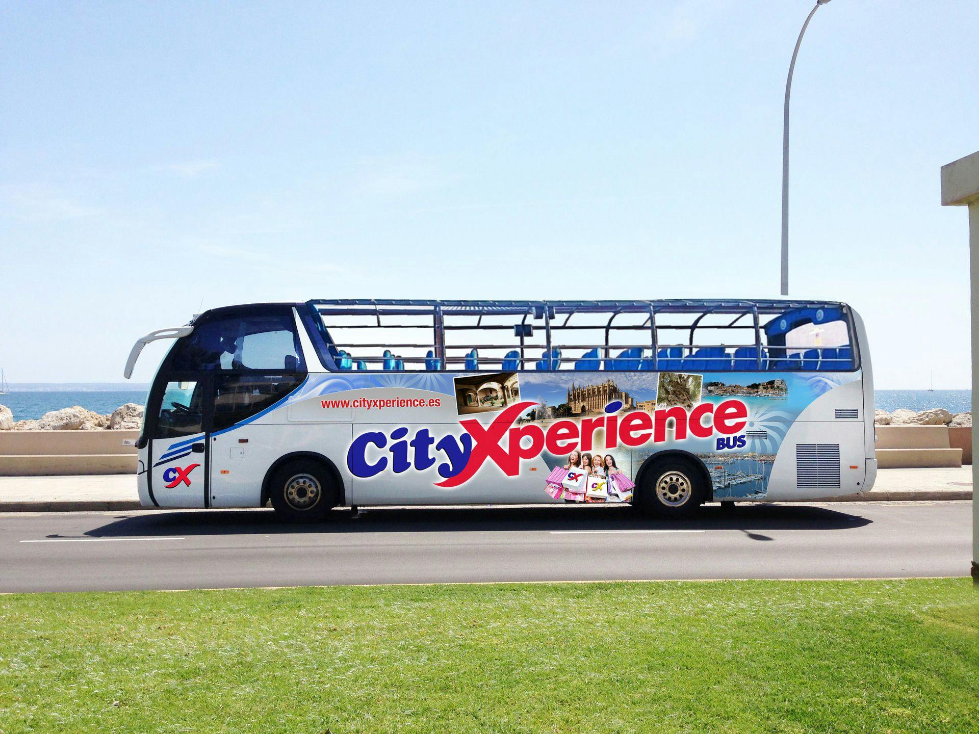 一辆白色双层City Xperience巴士停在草地旁边的道路上，车顶敞篷，图案丰富多彩。