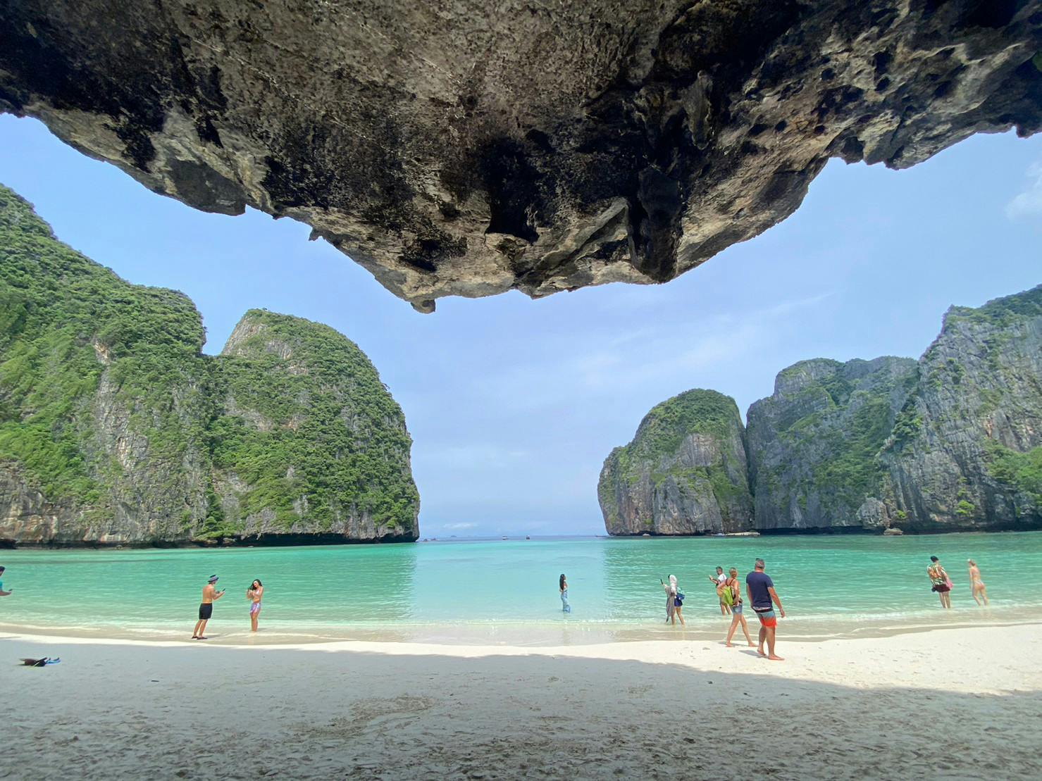 Des touristes profitent d'un lagon clair et peu profond avec des falaises calcaires en arrière-plan, vues depuis l'ouverture d'une grotte ombragée.