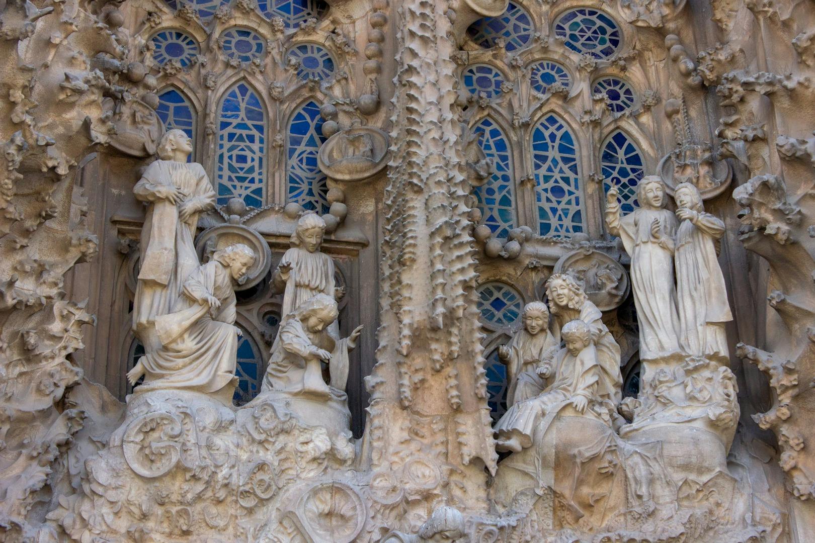 파란색 스테인드글라스 창문을 배경으로 건물 외관에 종교적 인물이 그려진 화려한 석조 조각품.