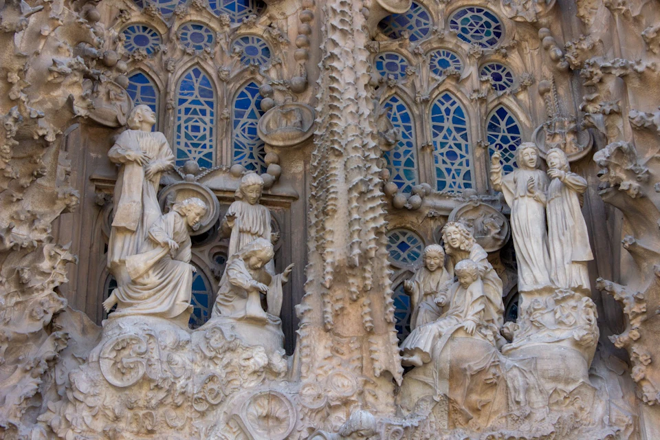 Ornate stone carvings depicting religious figures on a building facade, with blue stained glass windows in the background.