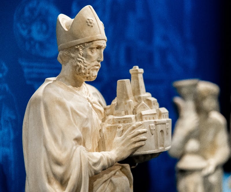 Una cornice nera che mostra una scultura di legno colorata, una ruota nera e una griglia di legno su uno sfondo scuro.