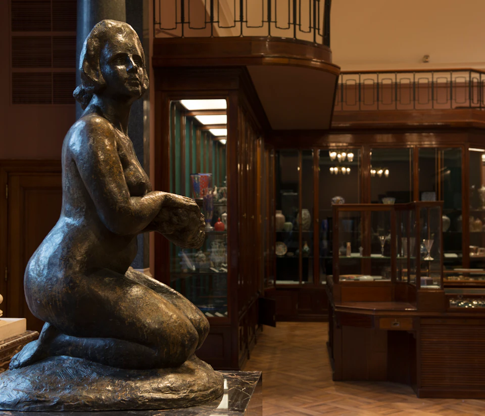 Kneeling bronze statue in a dimly lit museum room with glass display cases and wooden flooring.