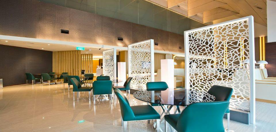 A modern lounge area with green chairs, glass tables, and decorative white partitions in a well-lit space.