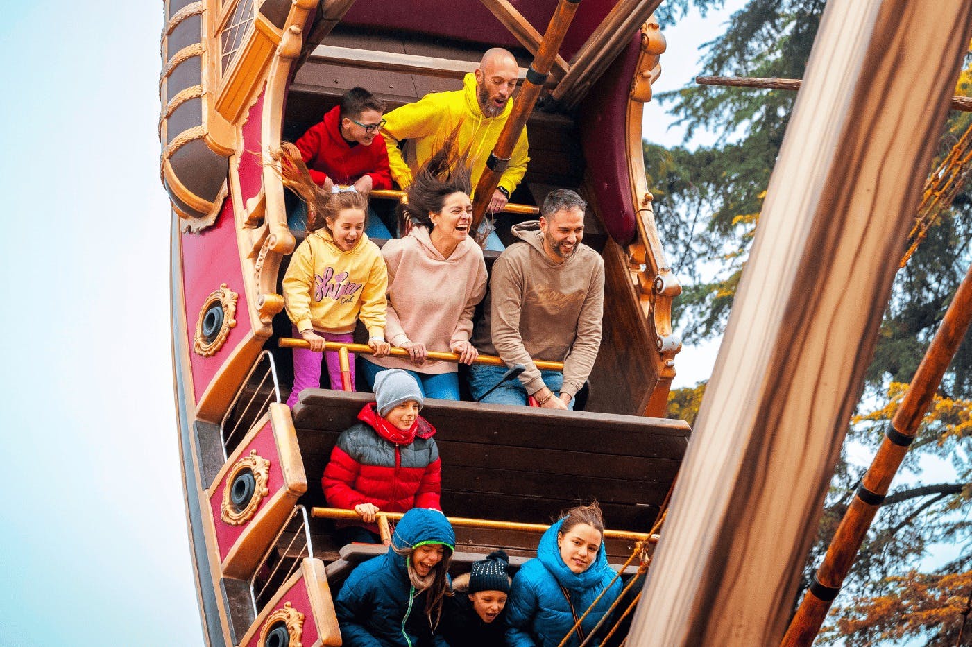 Άνθρωποι διαφόρων ηλικιών απολαμβάνουν μια βόλτα σε ένα πειρατικό πλοίο, όλοι φορούν χειμωνιάτικα ρούχα και εκφράζουν ενθουσιασμό.