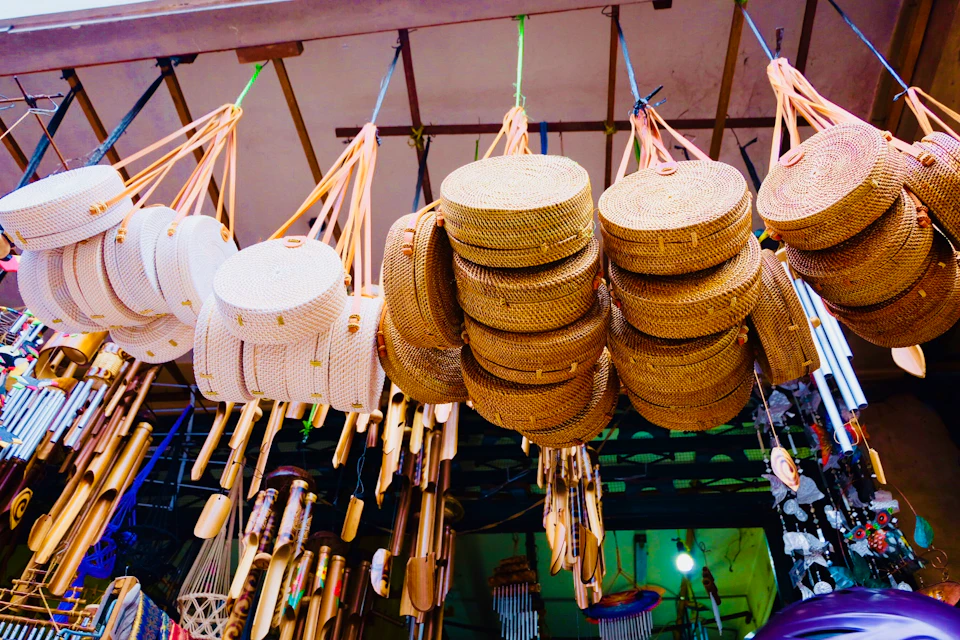 Stacks of woven straw hats hanging in a shop, surrounded by various wooden and bamboo crafts.
