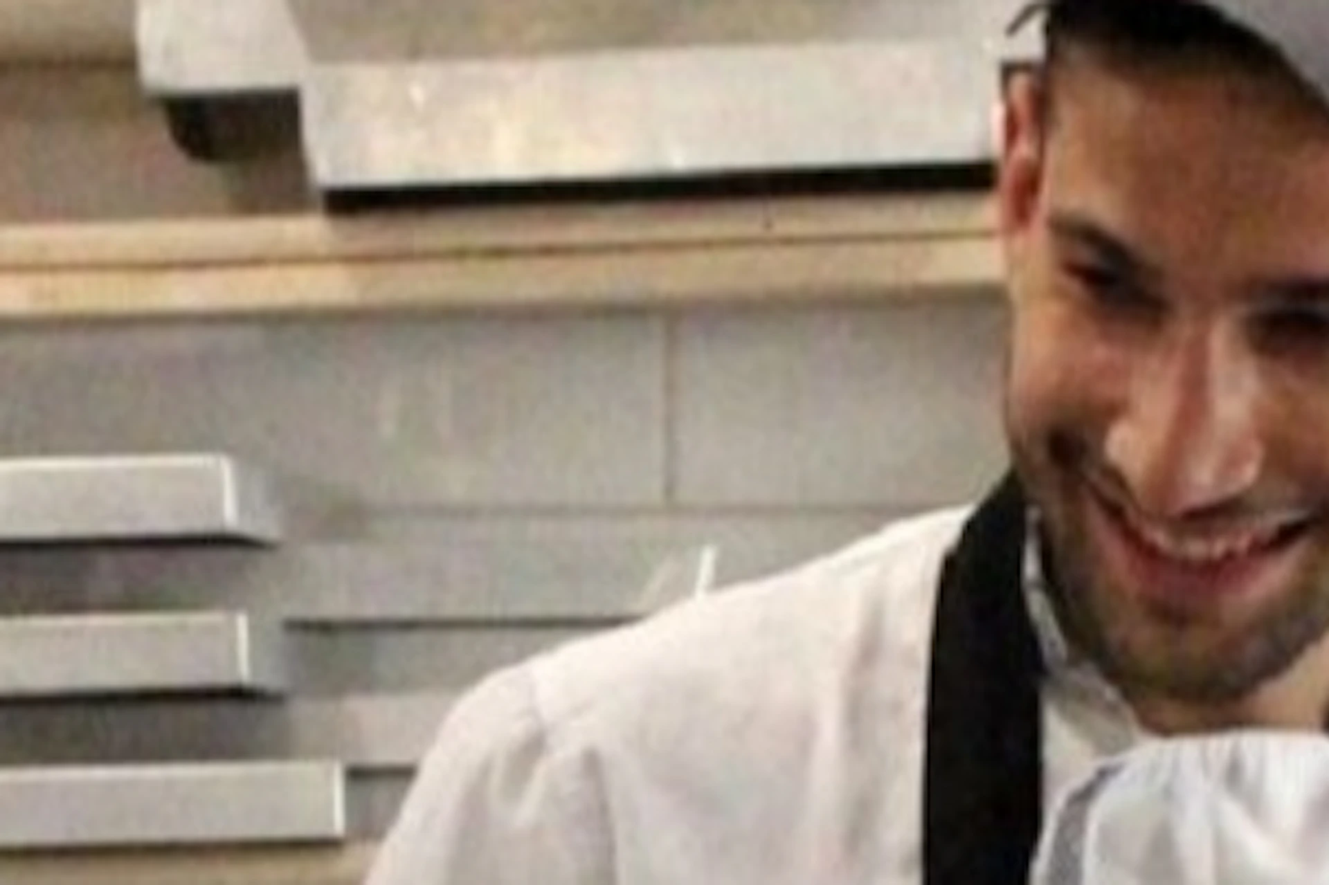 Three people wearing aprons and hairnets are smiling and cooking together in a kitchen, surrounded by bowls and utensils.