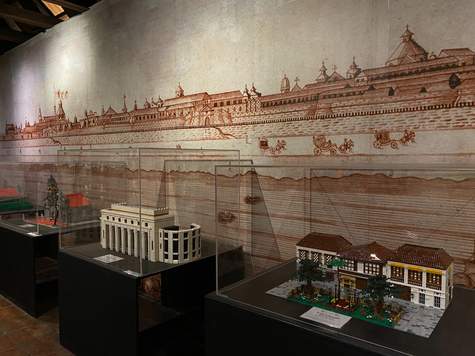 A display of historical miniature models in glass cases, with a detailed wall mural of an old cityscape in the background.