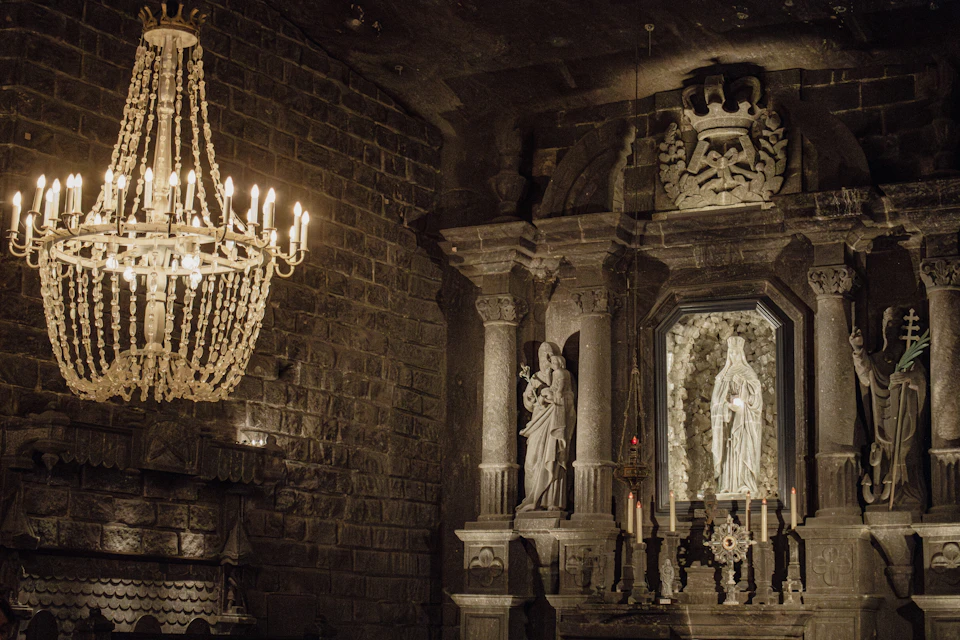 A dimly lit stone chapel interior featuring a chandelier, statues, and a carved altar with candles.