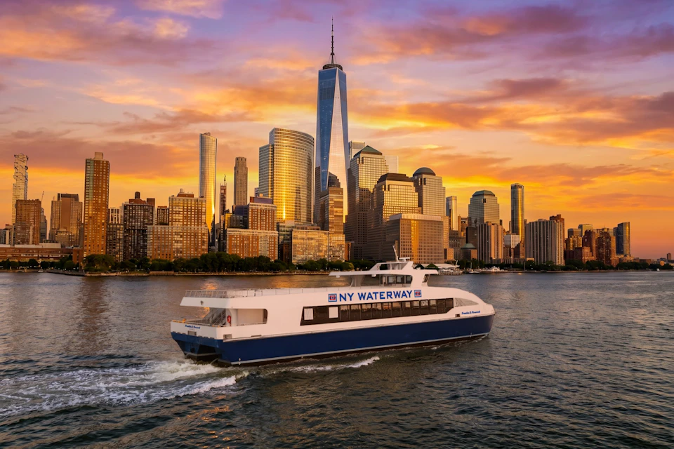 A ferry labeled 'NY Waterway' travels on water with a city skyline and sunset in the background.