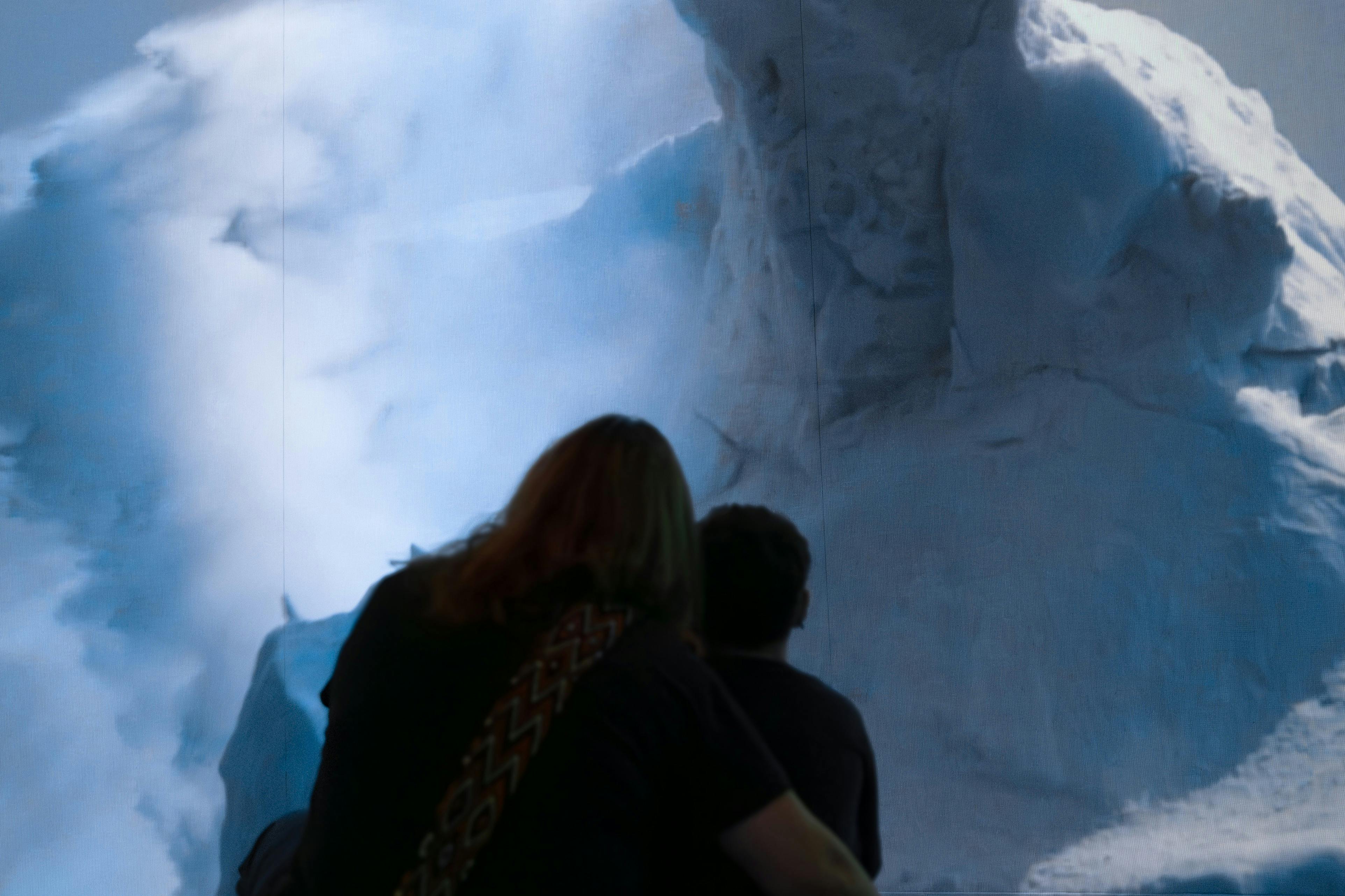 Dva lidé tváří v tvář ledové, zasněžené krajině s velkými útvary a zamračenou oblohou v pozadí.