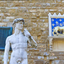 Närbild på Michelangelos David-staty bredvid en gyllene lejonskulptur på en blå, utsmyckad bakgrund med stenväggar.