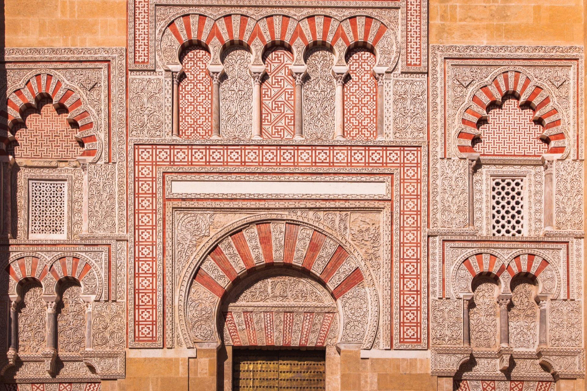 Intricate architectural detail featuring red and white arches, ornate carvings, and decorative patterns on a historic building facade.