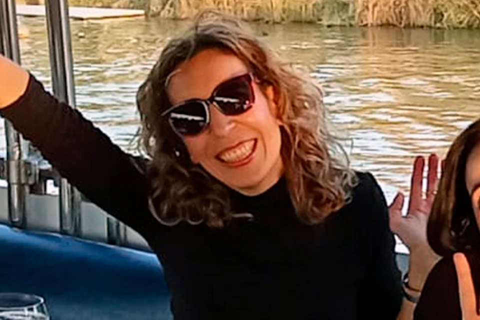Four women on a boat near a riverbank, smiling and posing at a white table with drinks and phones on it.
