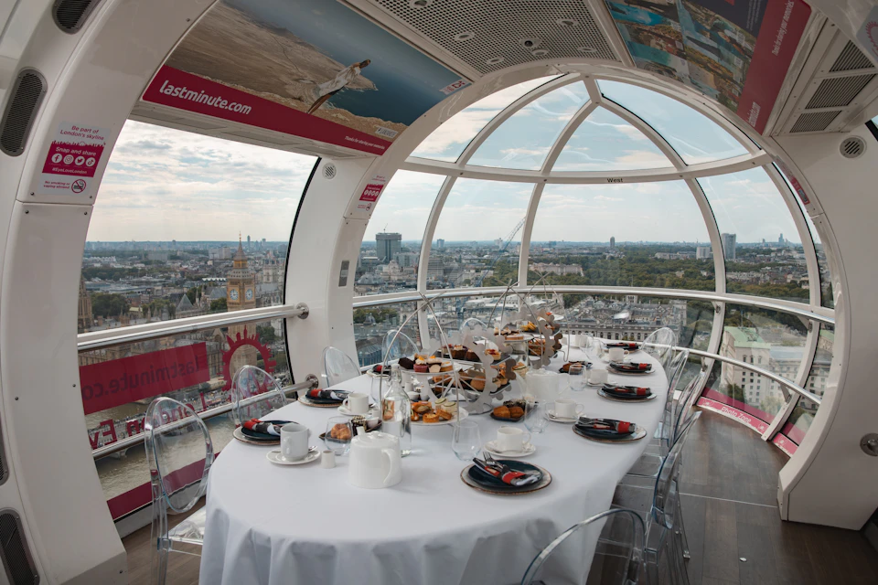 A table set for a meal with pastries and tea inside a glass-enclosed observation wheel pod overlooking a cityscape.