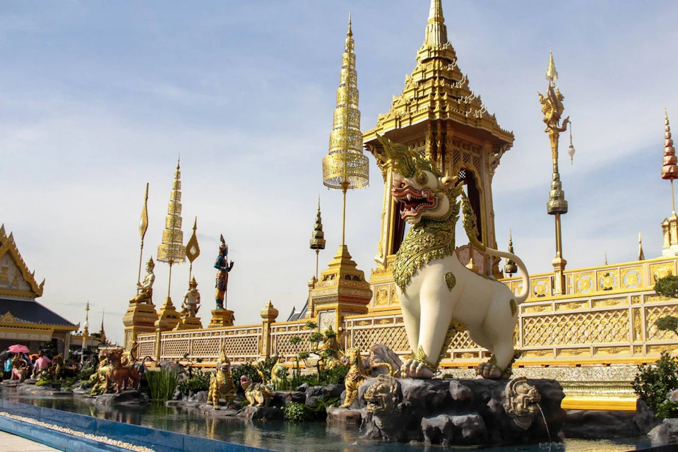An ornate Thai temple adorned with golden spires, intricate statues, and a large mythical creature sculpture in front.
