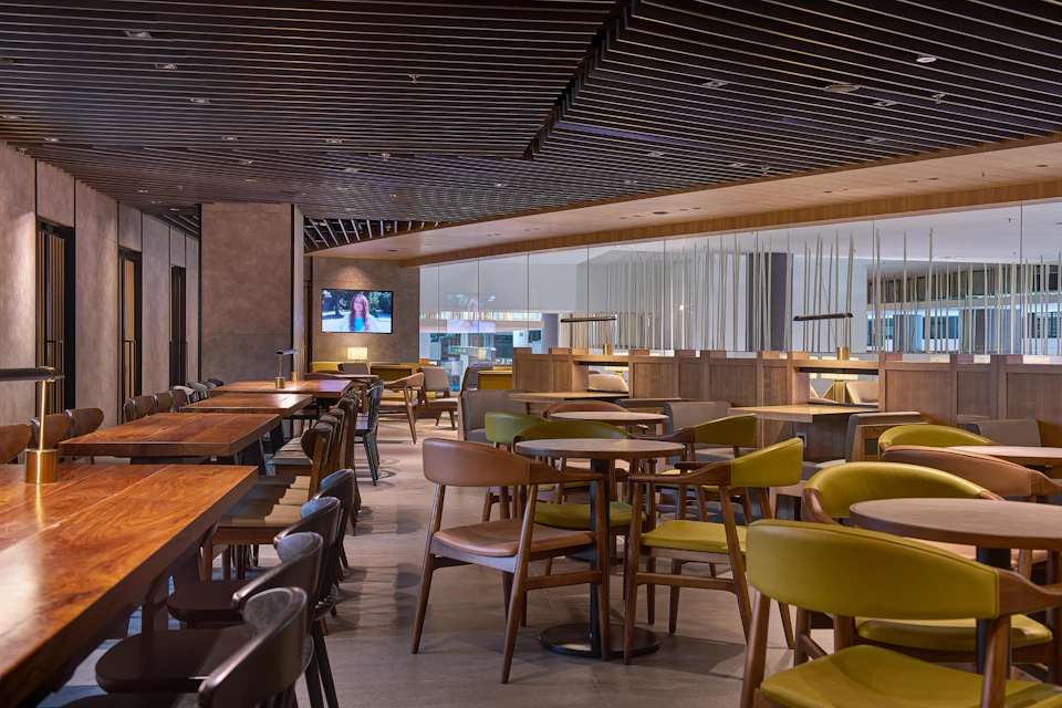 A modern restaurant interior with wooden tables, chairs, and a TV screen on the wall.