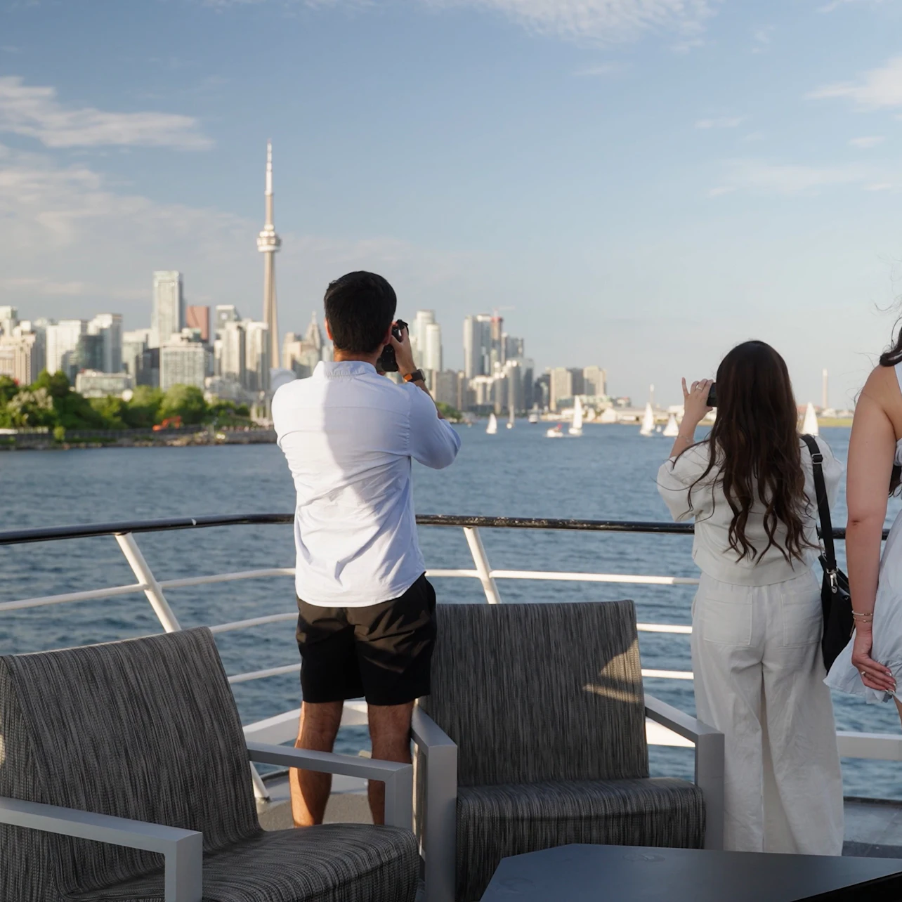 People on a boat deck photographing a city skyline with a prominent tower across a body of water.