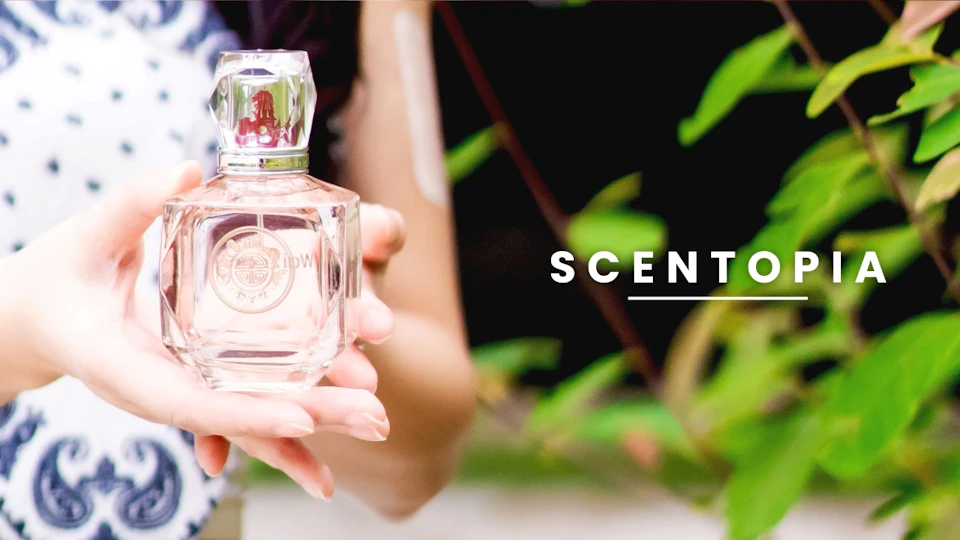 Close-up of a person holding a perfume bottle outdoors, with the word "SCENT" displayed to the right.