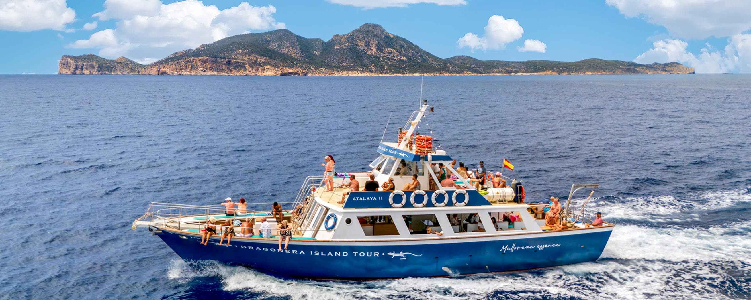 Turisti a bordo di una barca turistica blu denominata "ATLAYA II" vicino a un'isola panoramica in una giornata di sole.