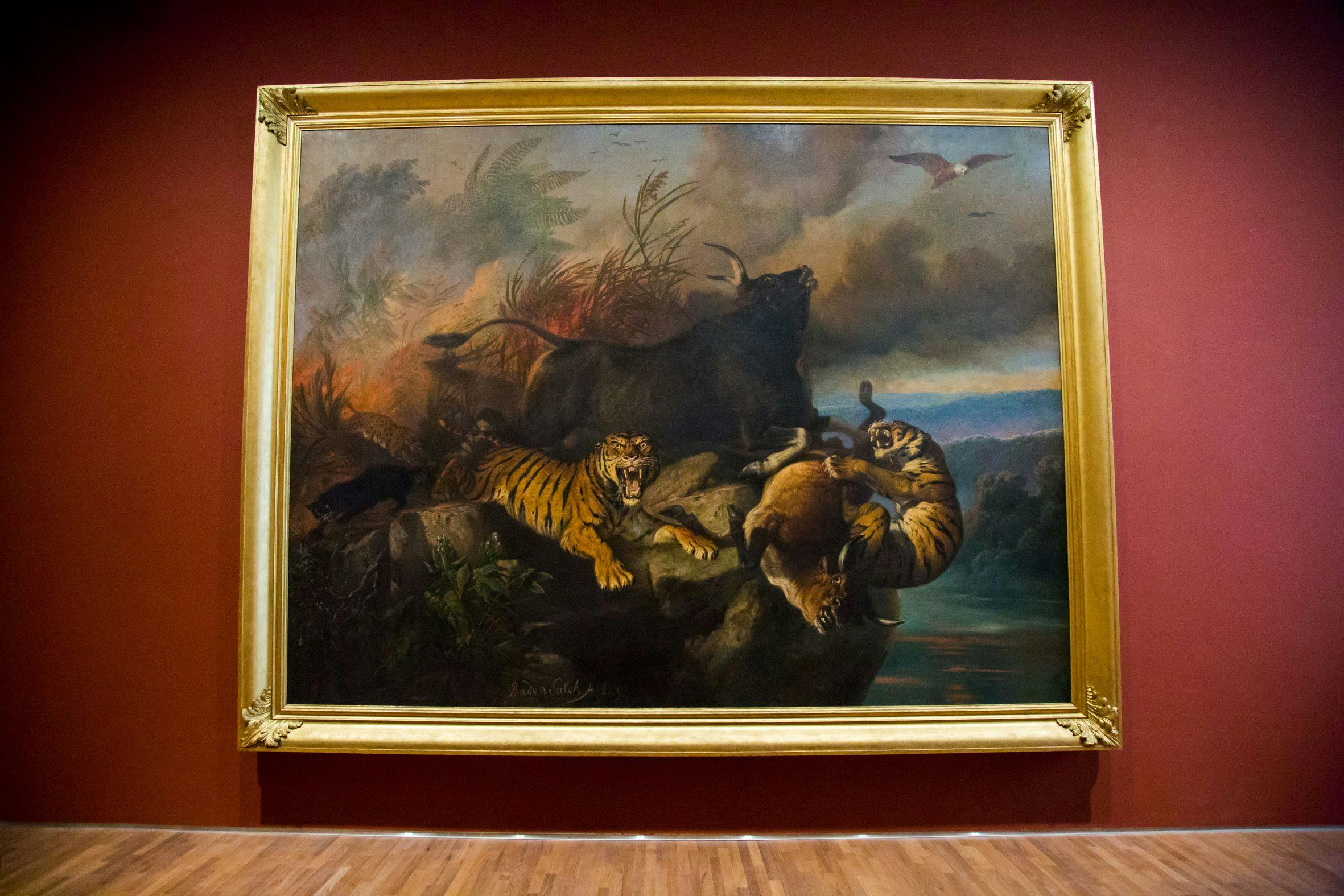 A painting depicting two tigers attacking a bison on a rocky landscape, with dramatic skies in the background.