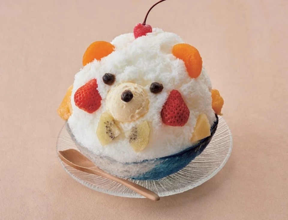 A bowl of shaved ice decorated to resemble an animal, with fruits arranged as features, and a cherry on top.