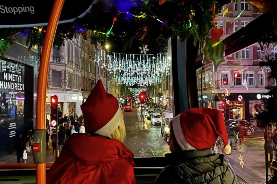 Two people in red Santa hats look out at a city street adorned with festive holiday lights.