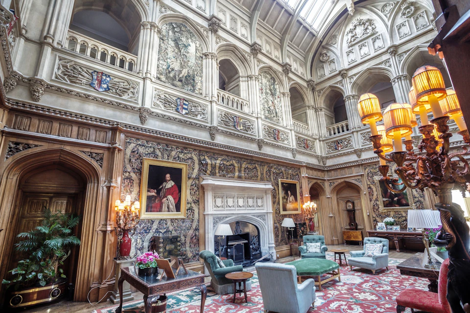 A grand, ornate room with a high ceiling, elaborate decorations, large paintings, and elegant furniture arranged around a fireplace.