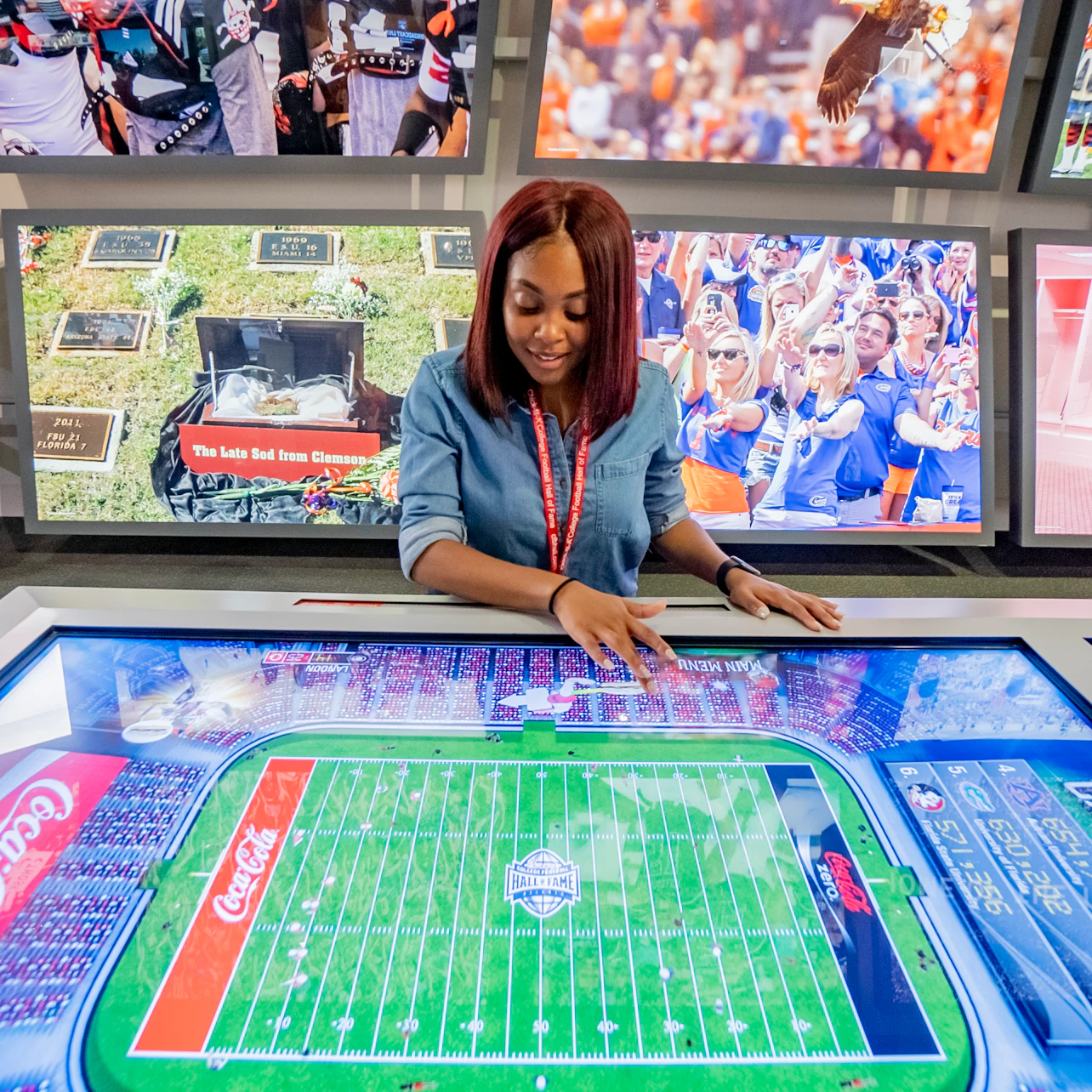 A woman interacts with a digital display of a football field, with large sports-themed images on the wall behind her.